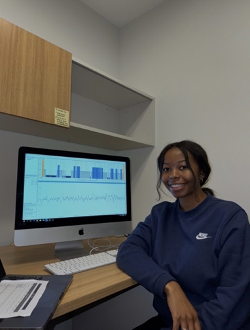 Payton smiles at the camera, while a computer screen behind her shows EEG waves.