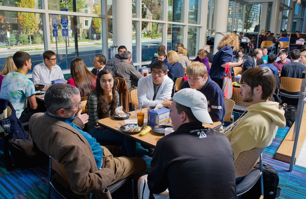 A large group of students and faculty in discussion at the dining hall.