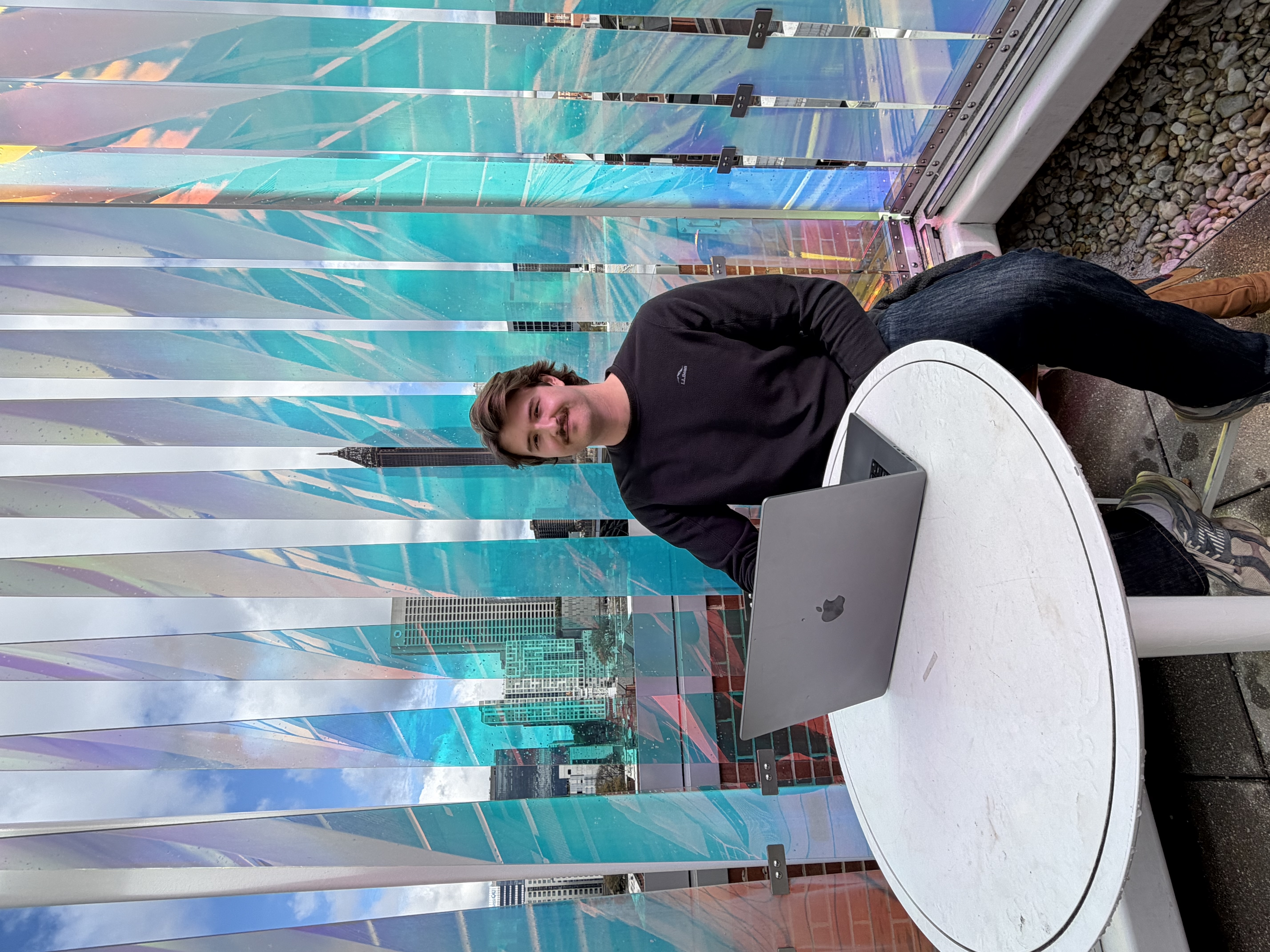 Eli sits in front of a colorful glass display, with a laptop on the table in front of him.
