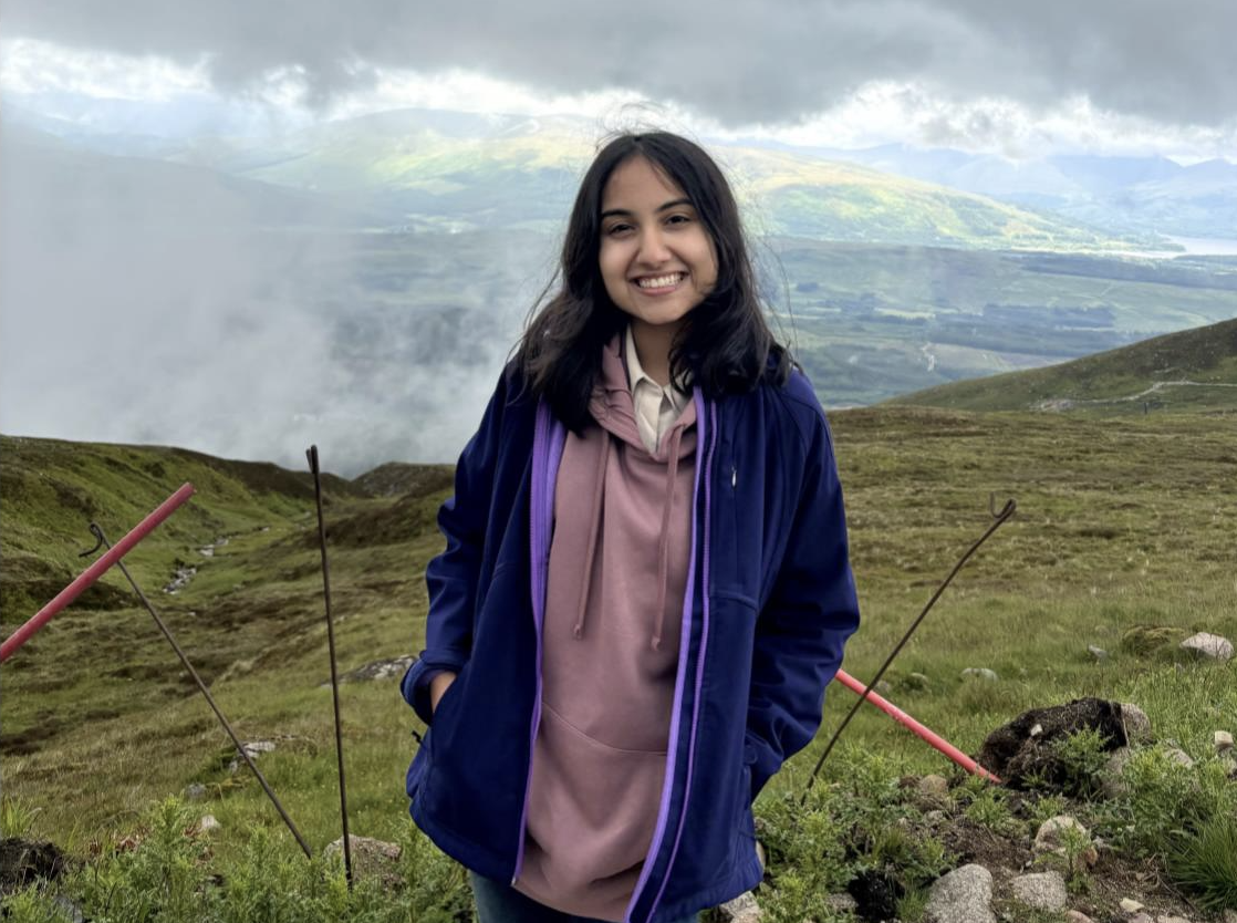 Shreya smiles at the camera, with a rainbow behind her.