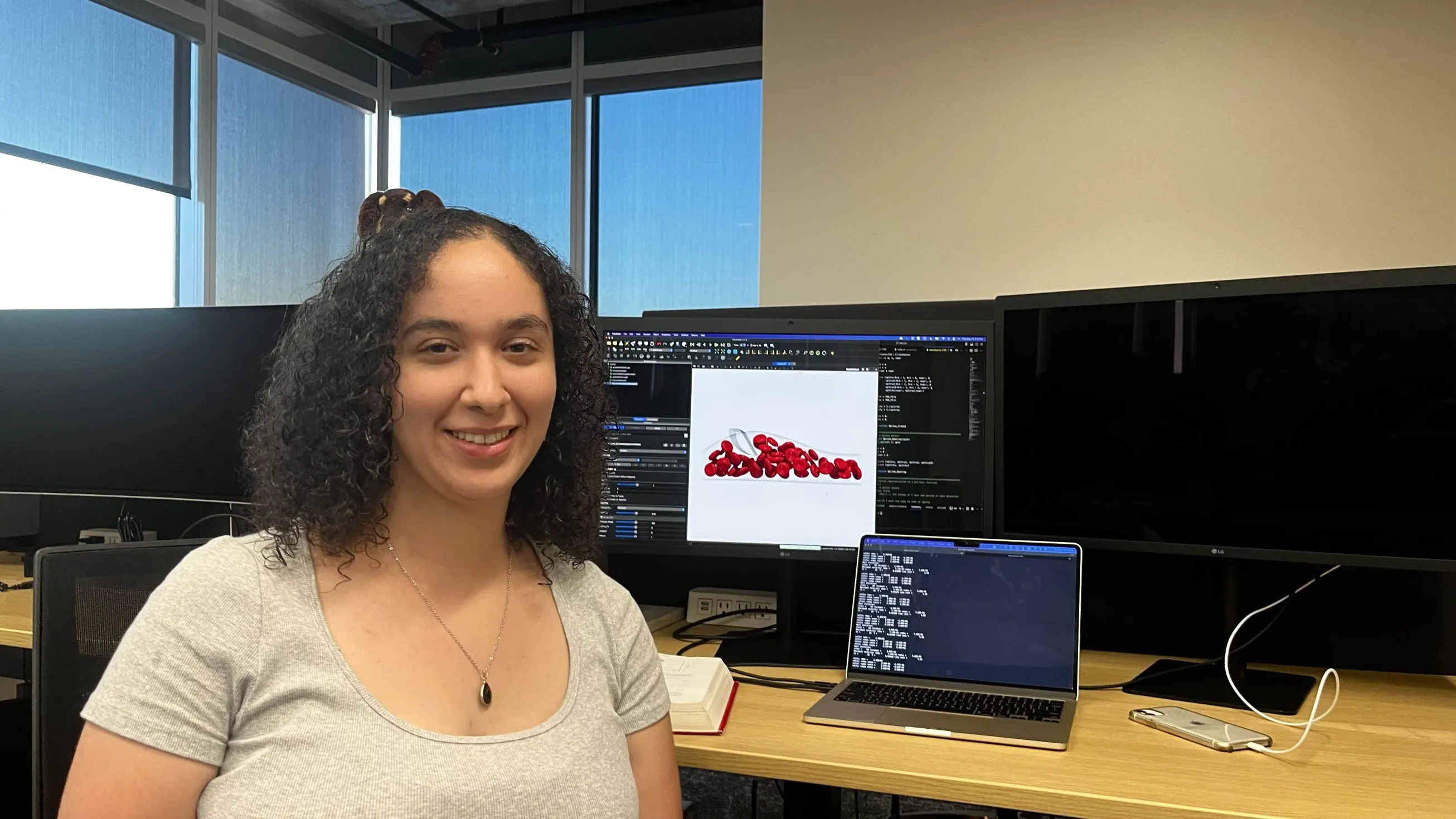 Suzan smiles at the camera, with a simulation on the computer screen behind her.